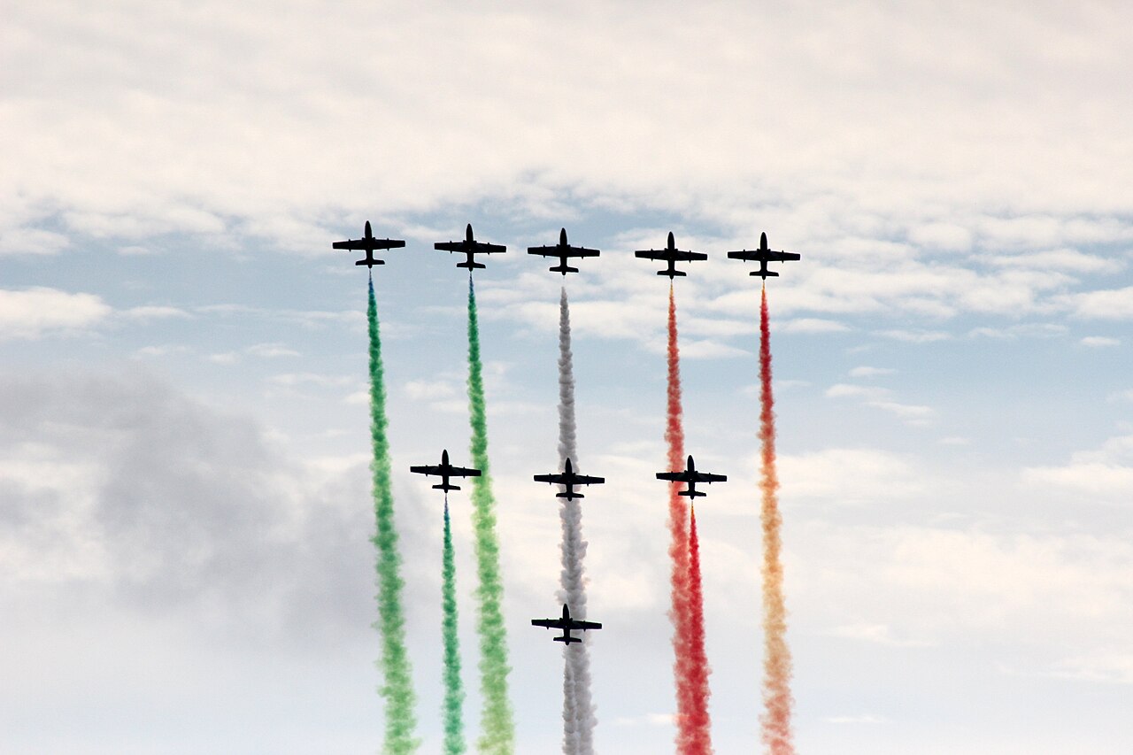 Nine jets flying in formation, trailing green, white and red smoke