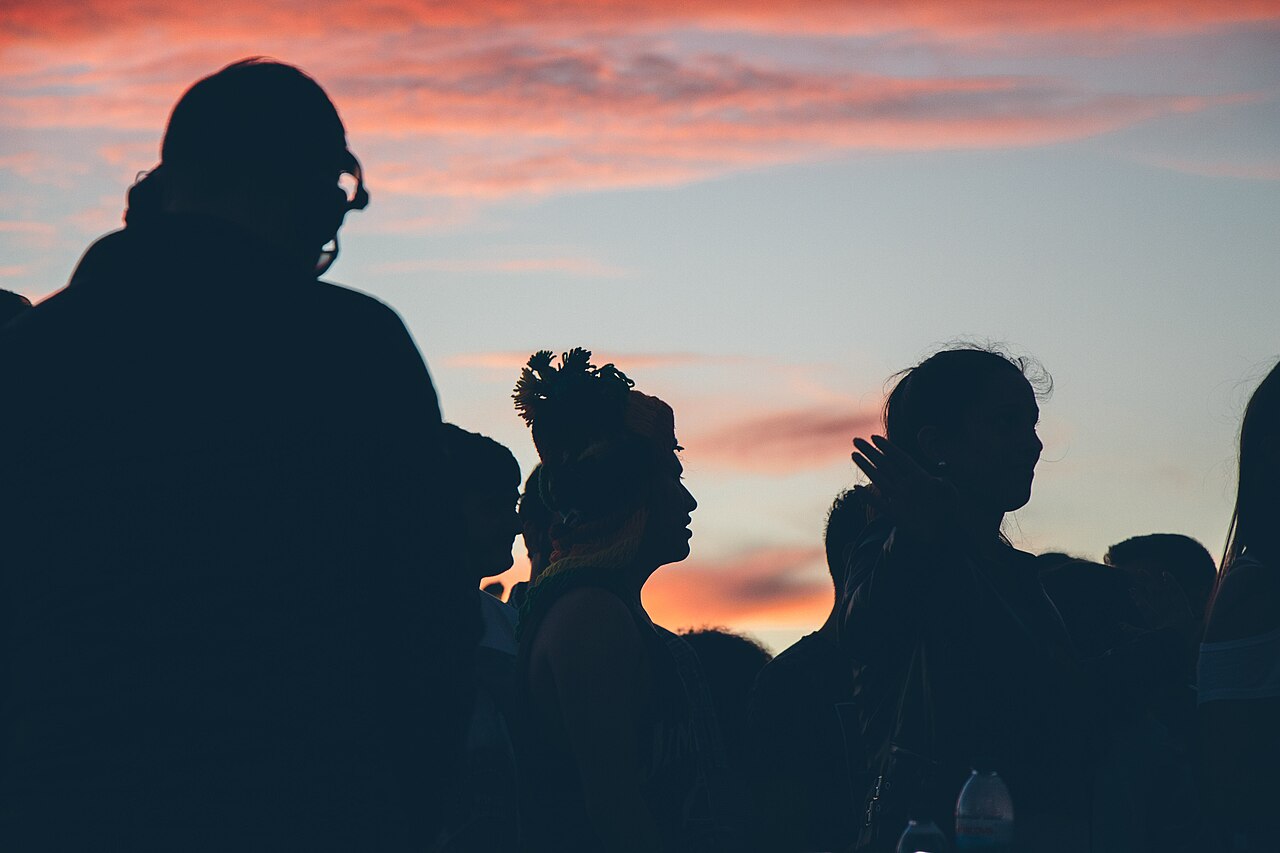 A festival crowd in silhouette against a sunset sky